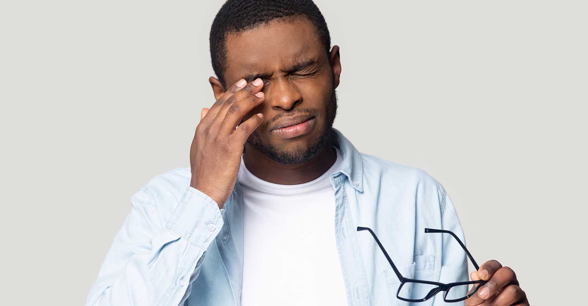African American man suffering from pain connnected with nasal disorder touching painful over-eye area with his hand and holding glasses in the other hand