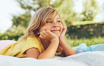 Cheerful child relaxing on a blanket in the park and enjoying summertime
