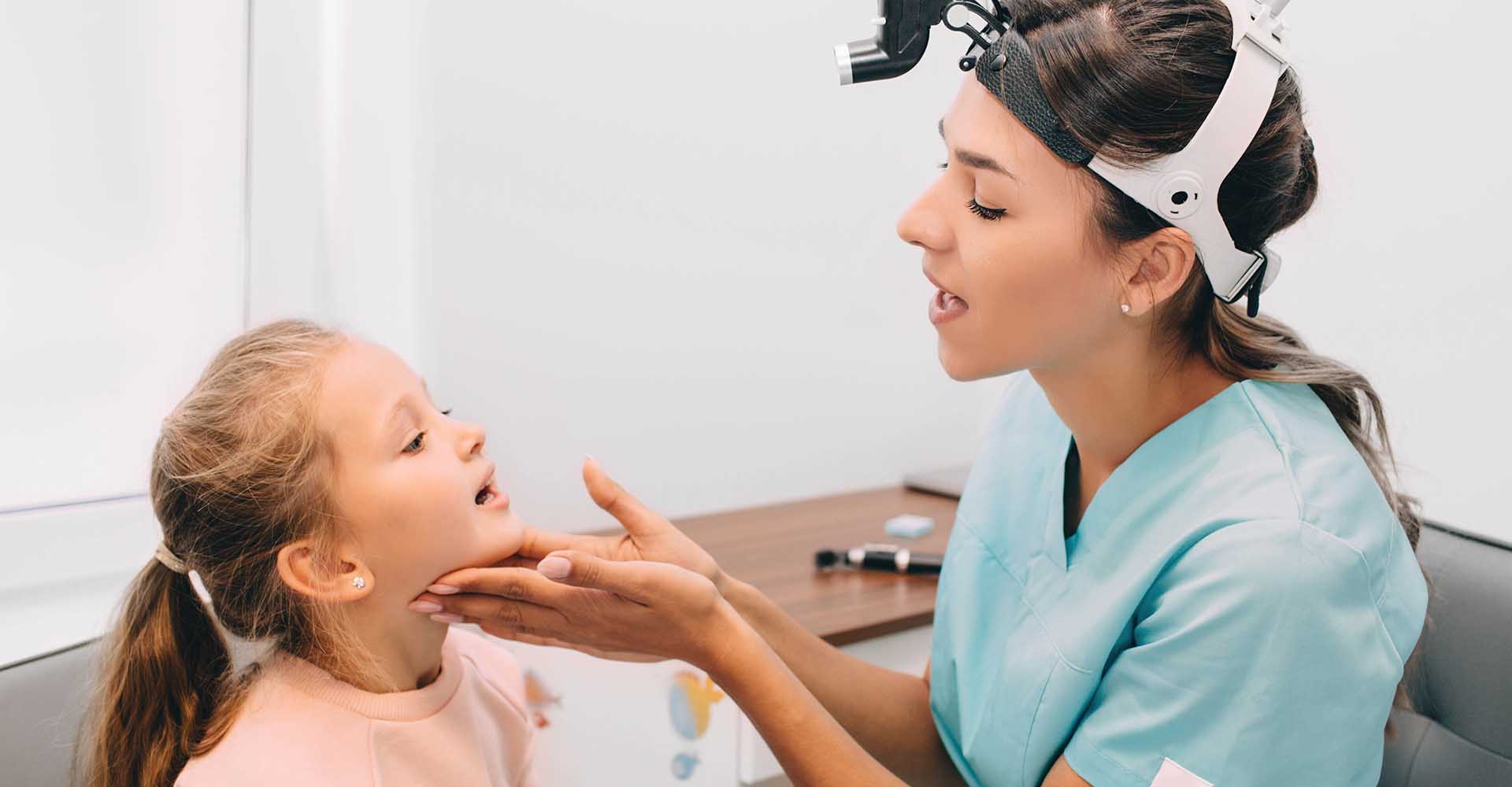 ENT doctor examining mouth of little girl at clinic