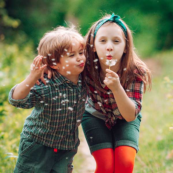 little boy and a girl blowing dandelion while playing in the garden