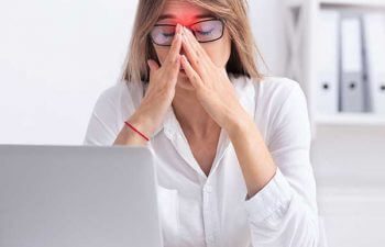 Businesswoman at work suffering srom sinus pain touching her nose and with both hands