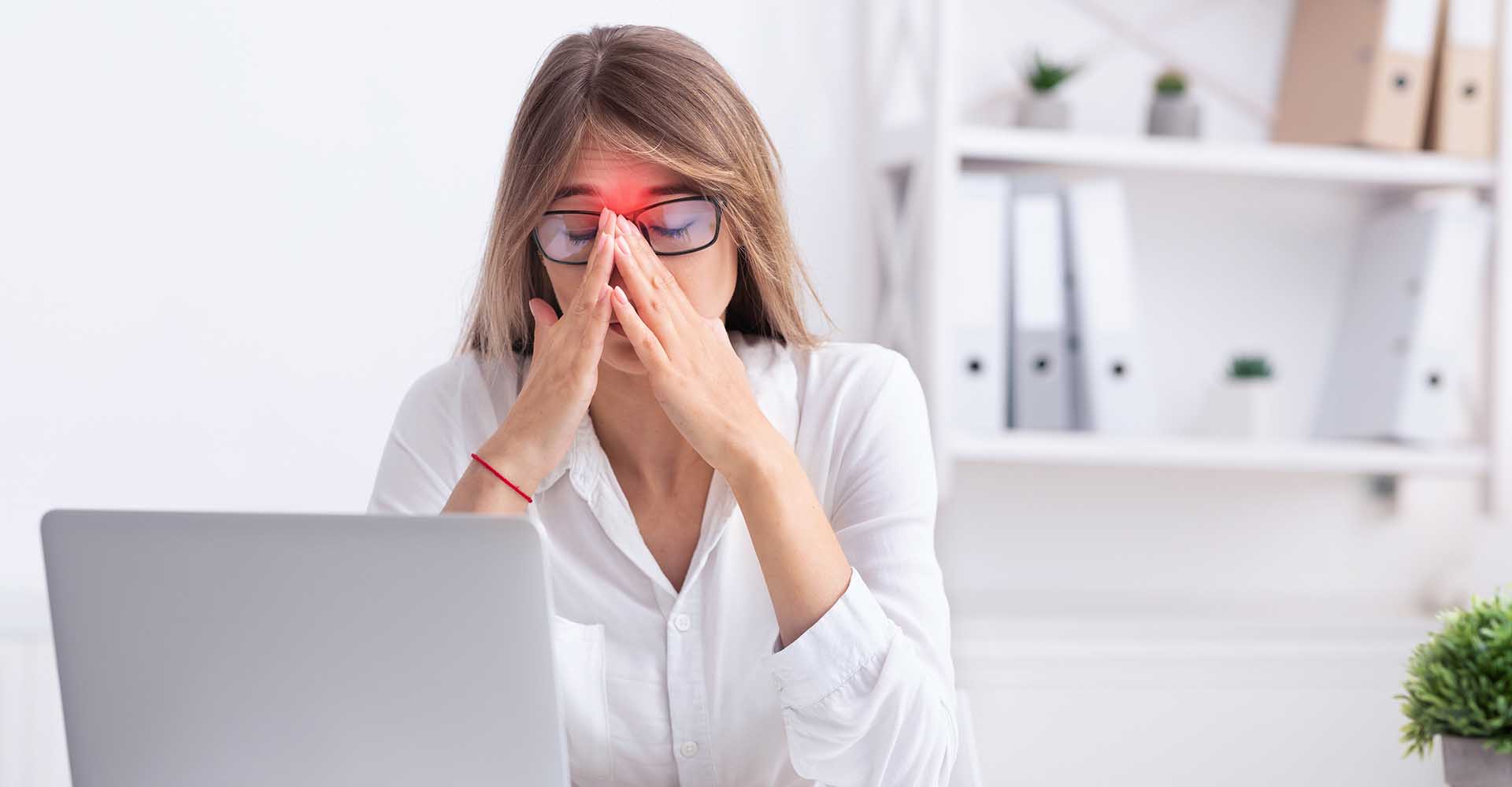 Businesswoman at work suffering srom sinus pain touching her nose and with both hands